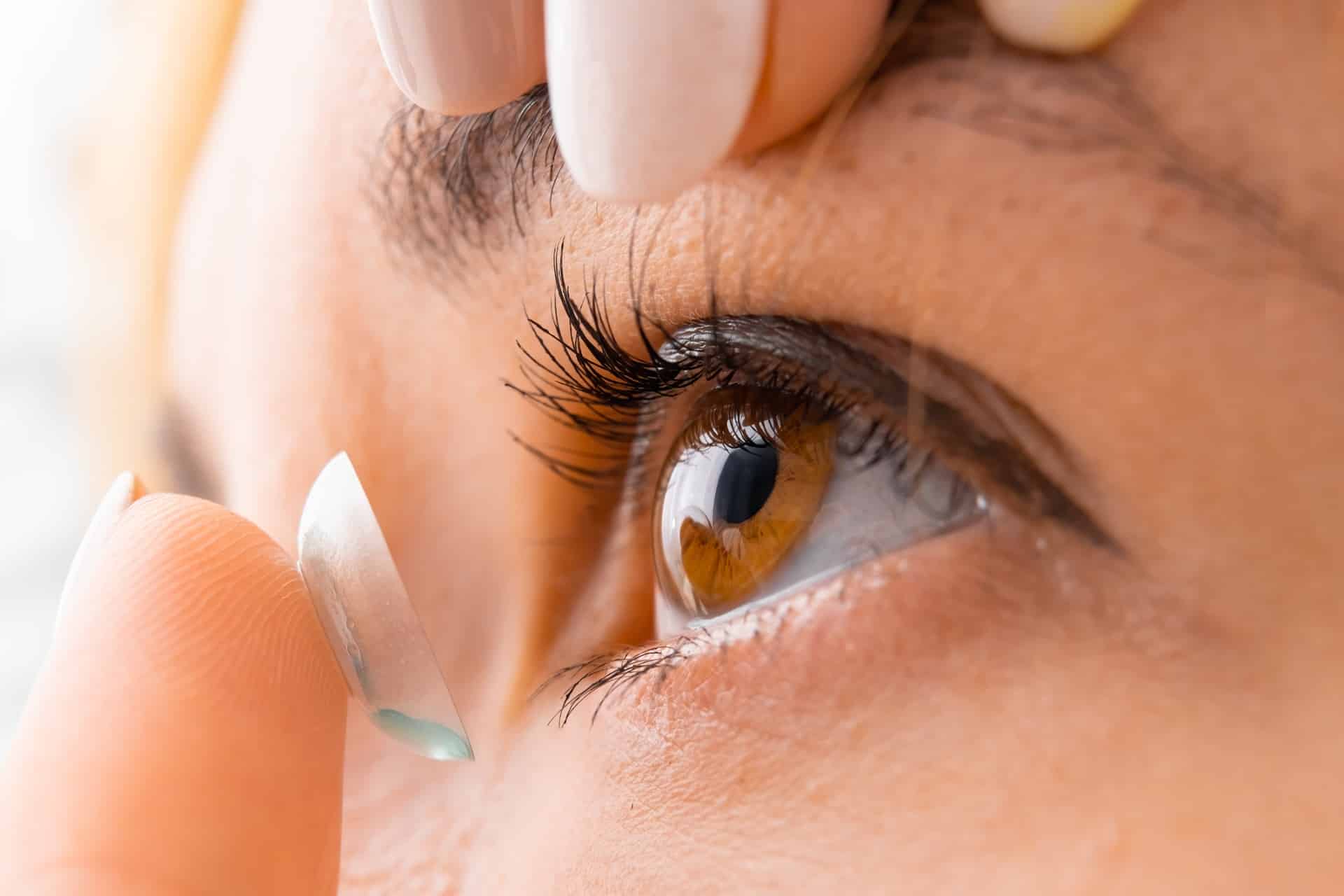 A woman putting a contact lens in and trying to decide between daily and monthly contacts.